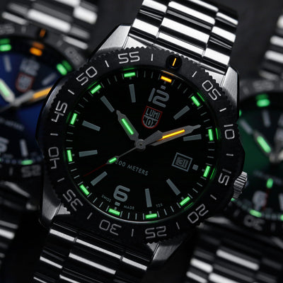 Close-up of a silver watch with a black face and green accents on a blurred background.