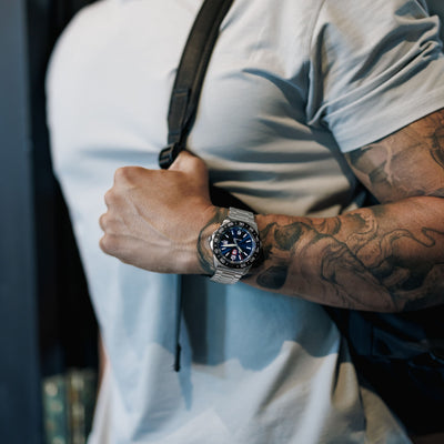 Person wearing a watch with tattoos on their arm, blurred background